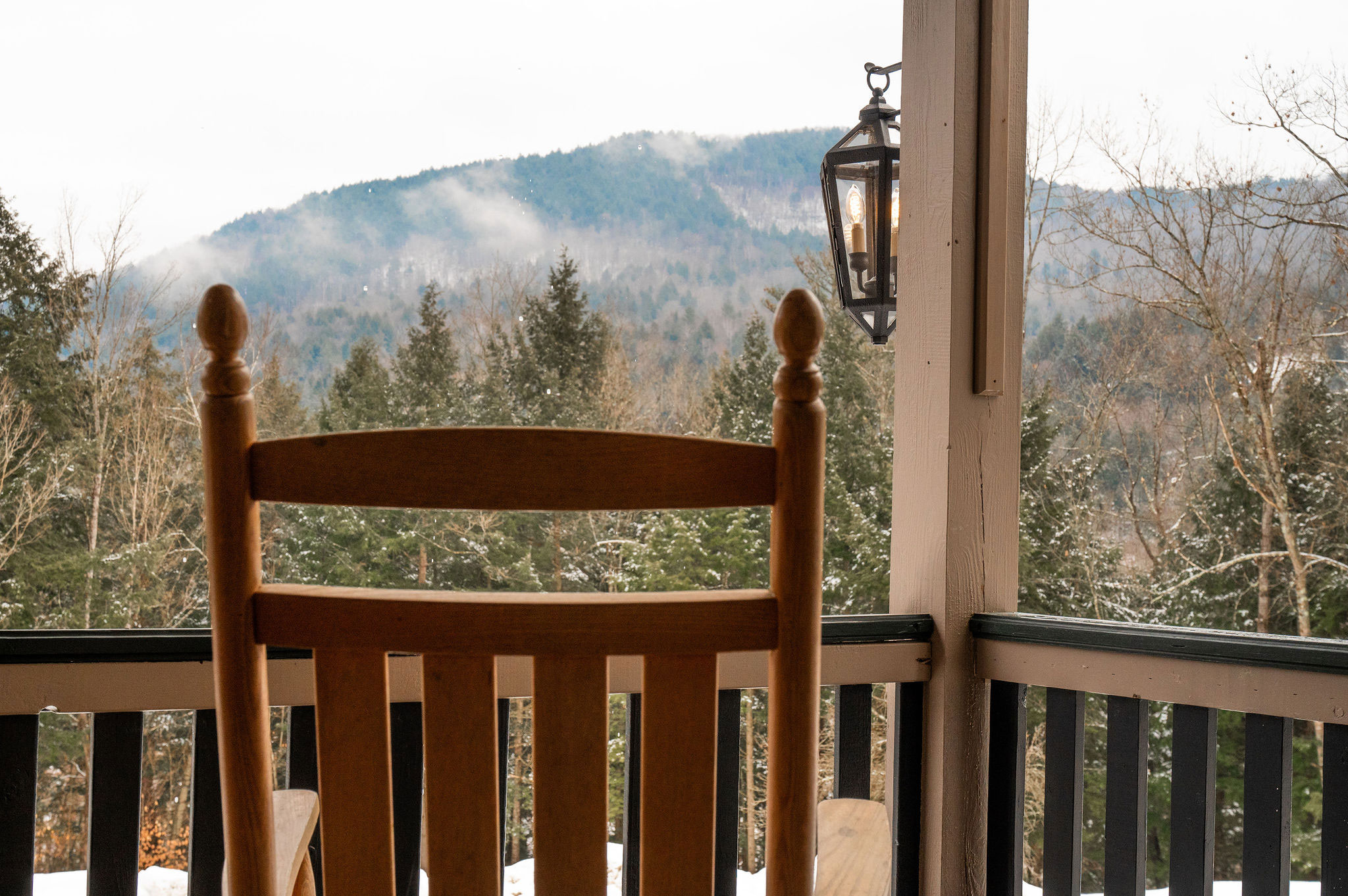 A detail of a rocking chair pulled up to the veranda rail and looking out on a winter landscape.