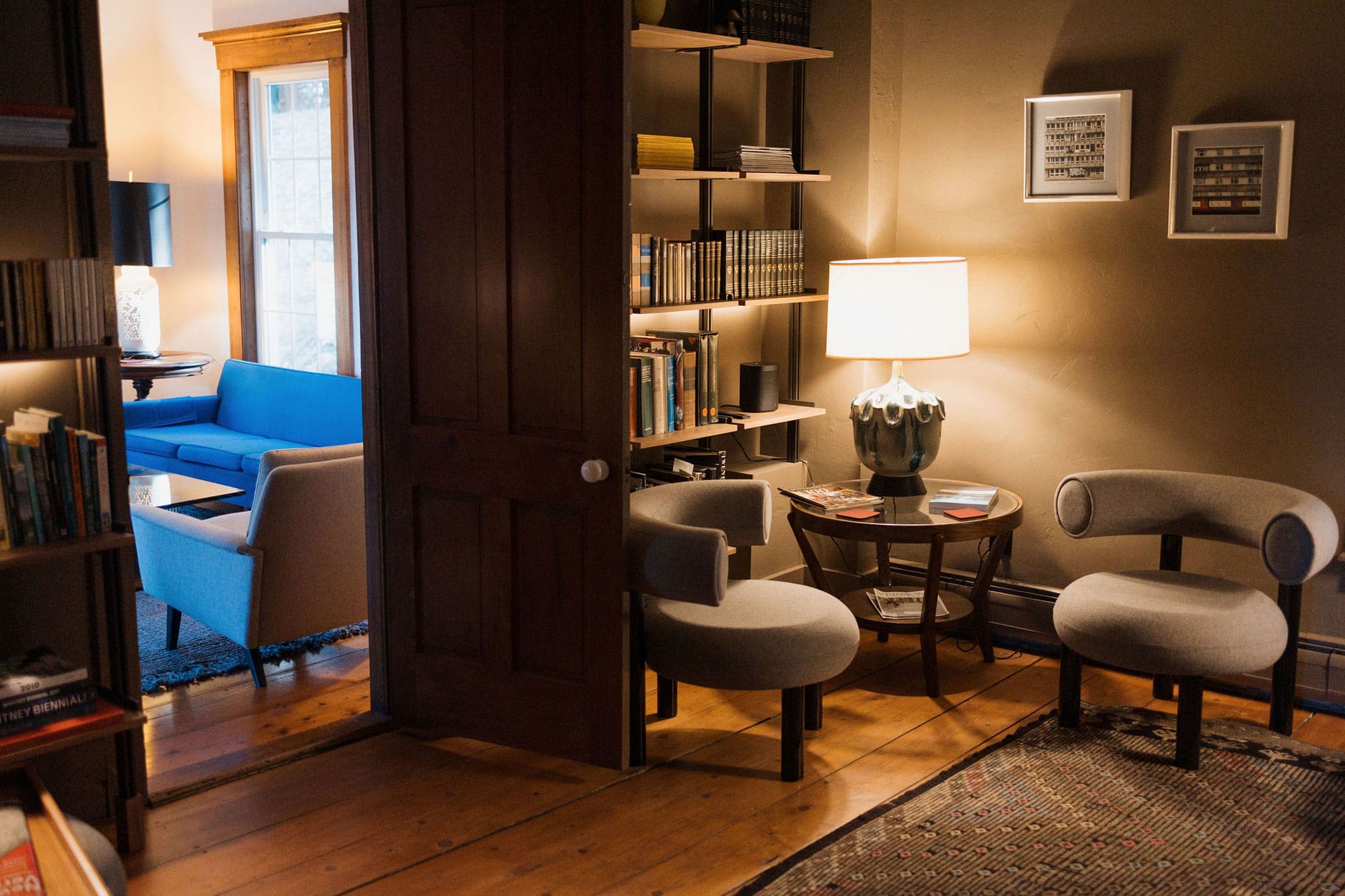 PeaksAndPearlsPhoto-128-clubroom The brightly lit reading corner of the Library, with two upholstered grey armchairs flanking a table with a lamp, and an open door leading to the parlor.