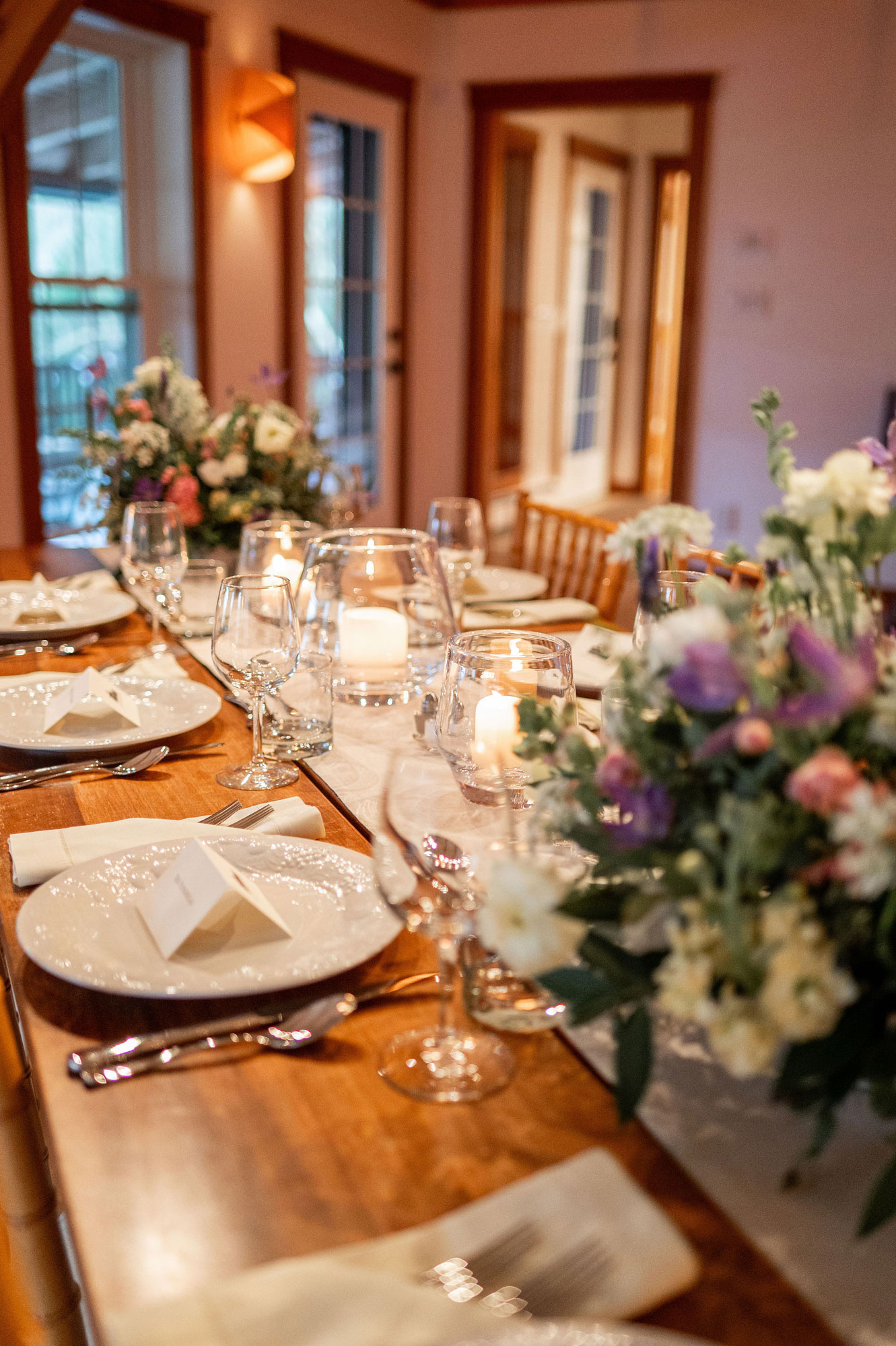 The Cobble House wedding dinner A table in the Music Room set with a large centerpiece of flowers, and fine dishes, cutlery, and glassware.