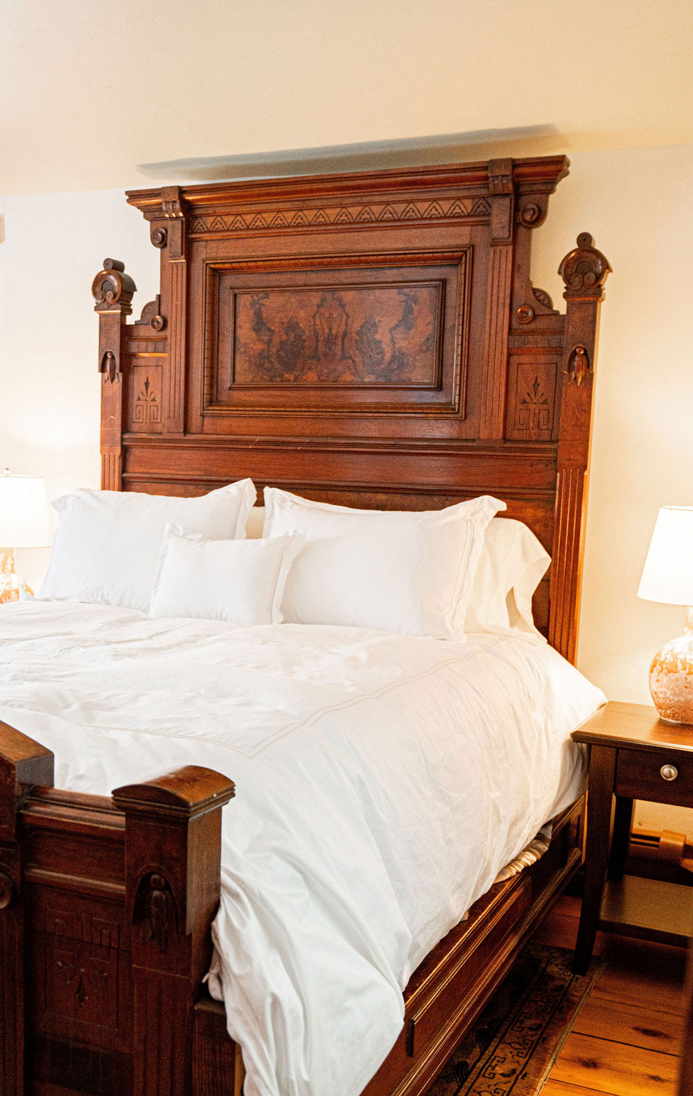 The Cobble House Victorian bedroom A large carved bed headboard and white bed linens and pillows