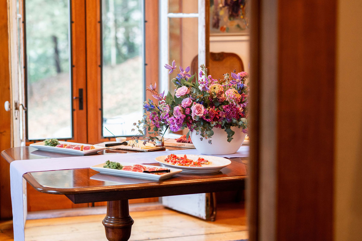 The Cobble House wedding dining room The Cobble House dining room table seen from the doorway, with platters of appetizers and an a large centerpiece with purple flowers.