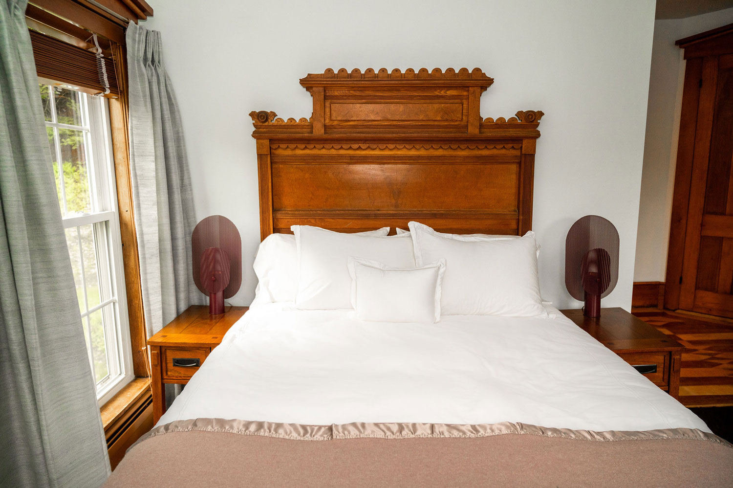 A large bed with a carved wooden headboard next to a large window with sage green curtains