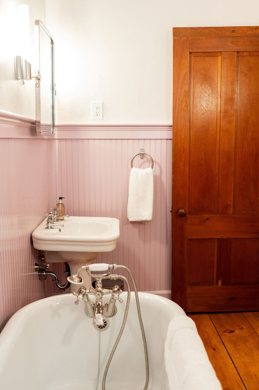 A corner of the Woodland bathroom with an old fashioned white tub, sink, and pink walls.