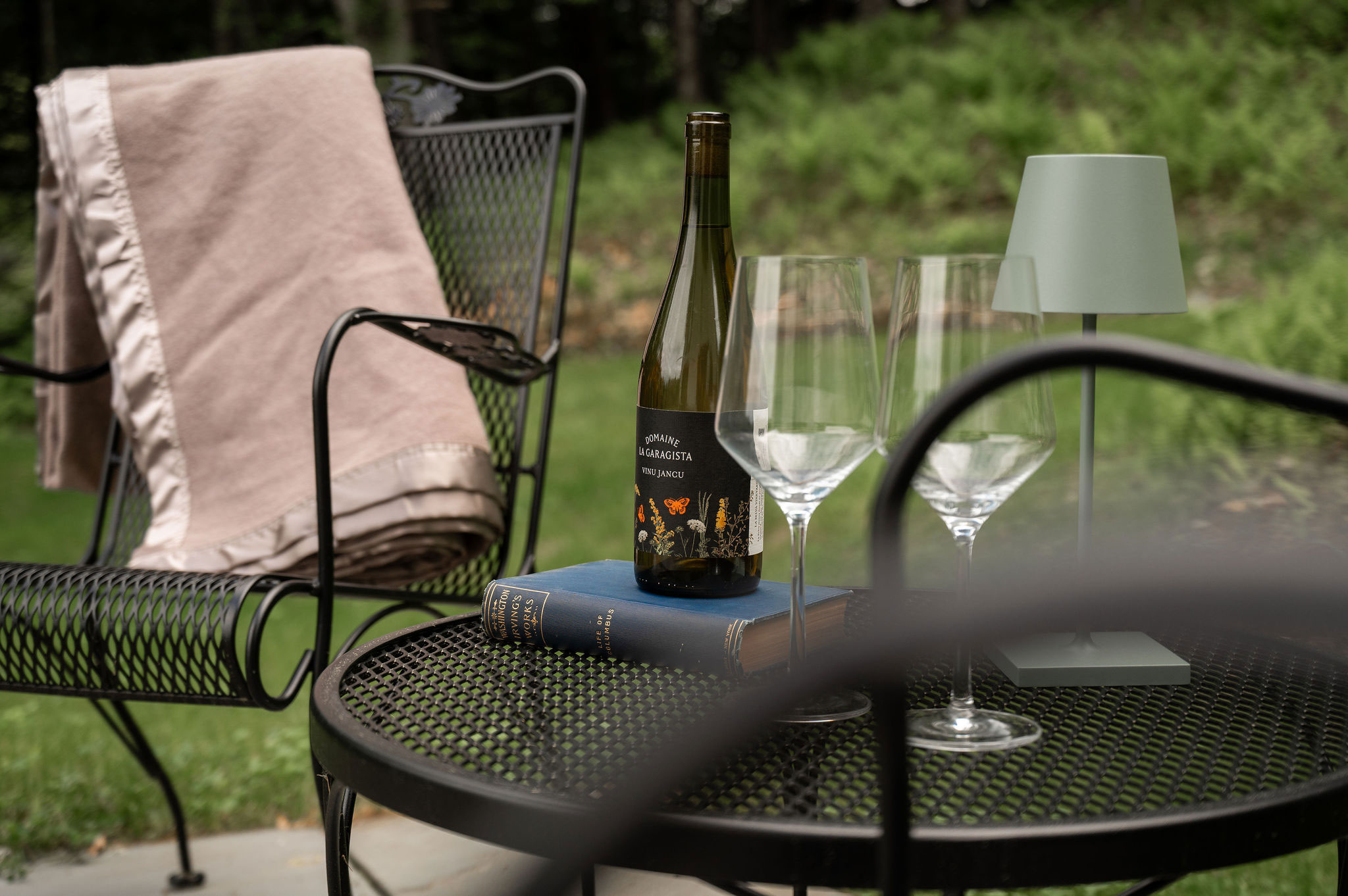 A bottle of wine and two glasses on a black wrought iron table on the bluestone terrace at The Cobble House