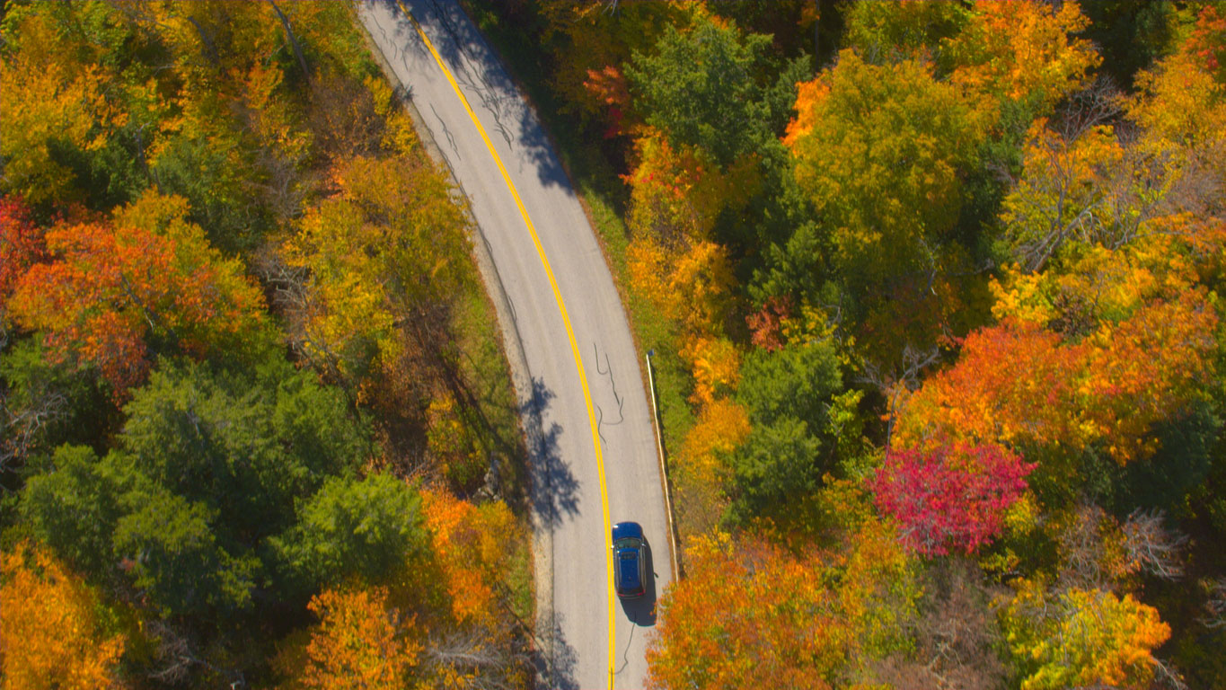 Aerial view of a car driving on a winding road through autumn foliage